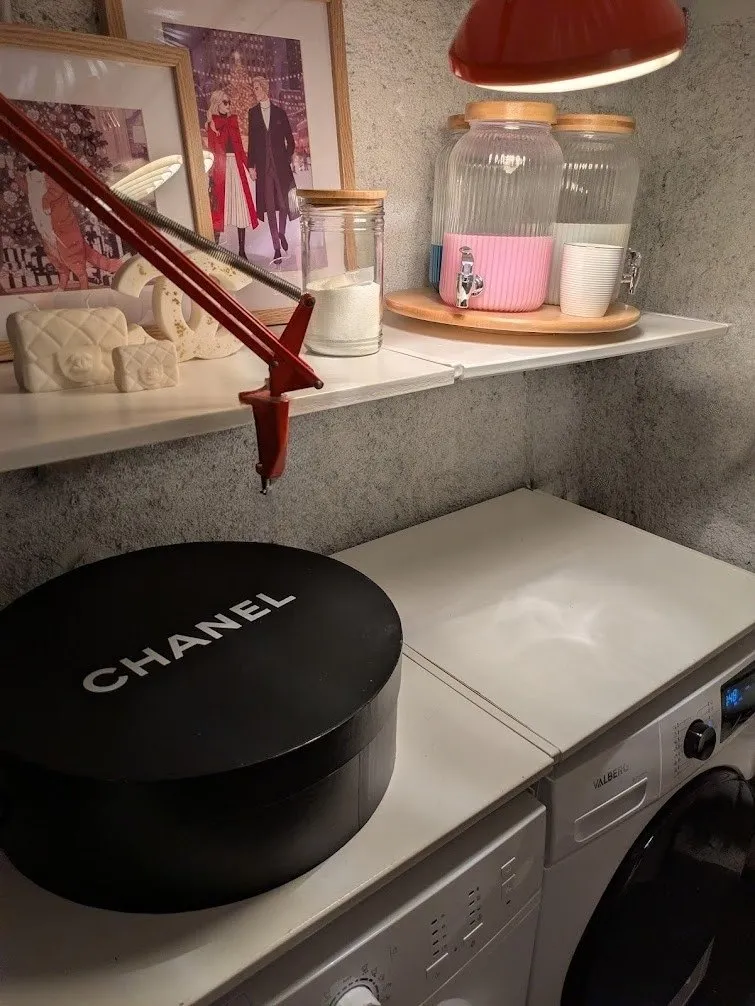 La boîte à chapeau ronde Chanel, posée sur la machine à laver, dans la lingerie