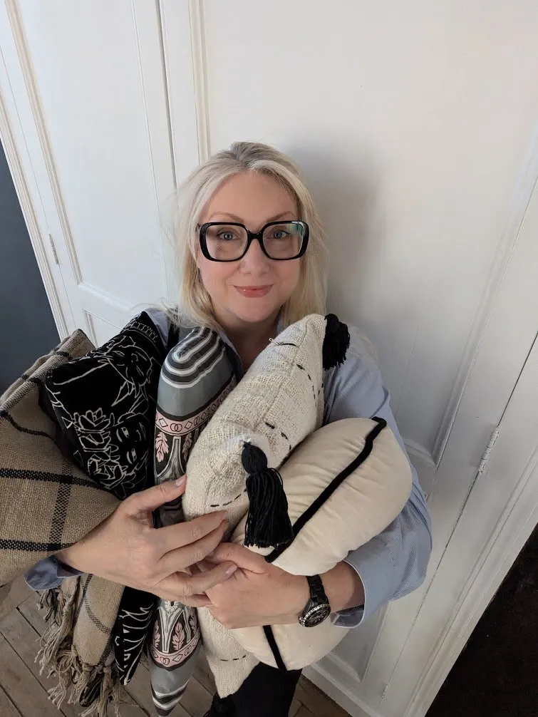 Aurélie, souriante, les bras chargés de coussins et d'un plaid