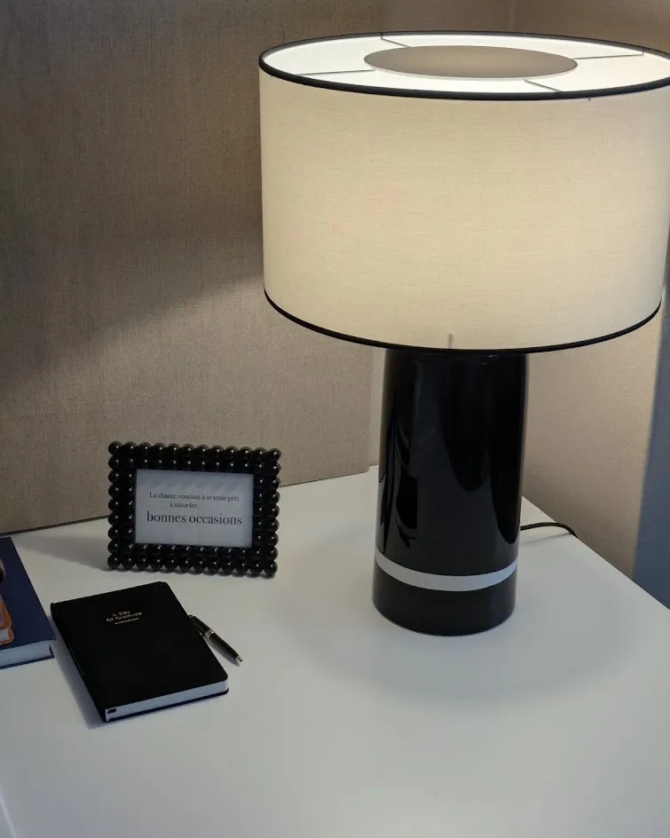 Une lampe, un cadre et un carnet noir sur une table blanche